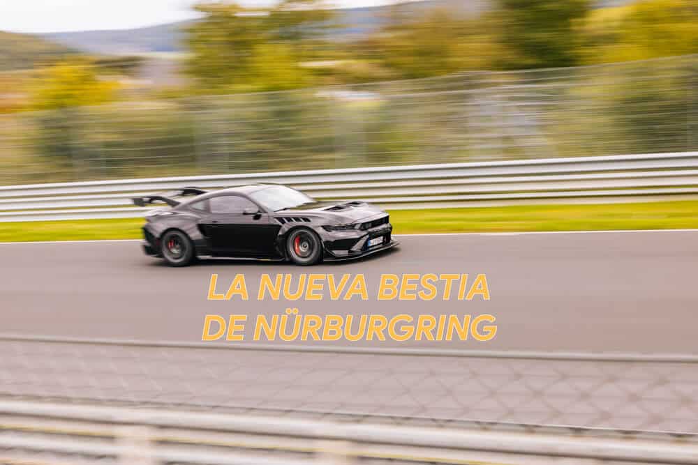 La imagen muestra un Ford Mustang GTD negro corriendo en el circuito de Nürburgring. El coche está capturado en movimiento, enfatizando su velocidad y capacidades de rendimiento. El fondo está ligeramente borroso, destacando el movimiento del coche. El texto "LA NUEVA BESTIA DE NÜRBURGRING" se muestra de manera prominente en primer plano, sugiriendo que este vehículo se está promocionando como un nuevo modelo de alto rendimiento en el famoso circuito de Nürburgring. Esta imagen es interesante y relevante porque muestra un coche de alto rendimiento en uno de los circuitos de carreras más desafiantes y renombrados del mundo.