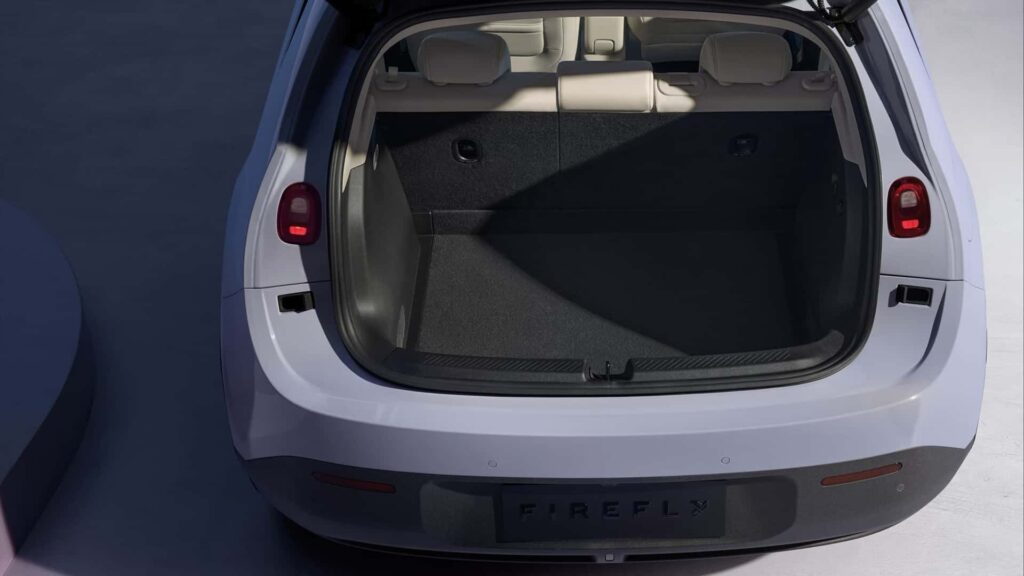 El maletero abierto de un NIO Firefly, un coche eléctrico. El maletero está vacío y tiene un interior limpio y espacioso con alfombrado oscuro. Los asientos traseros son visibles, y las luces traseras del coche están encendidas. El nombre de la marca del coche, 'NIO Firefly', es visible en el parachoques trasero. Esta imagen es interesante y relevante ya que destaca el espacio de carga y las características de diseño del maletero del coche, lo cual puede ser importante para los posibles compradores que evalúan la practicidad y la capacidad de almacenamiento del vehículo.
