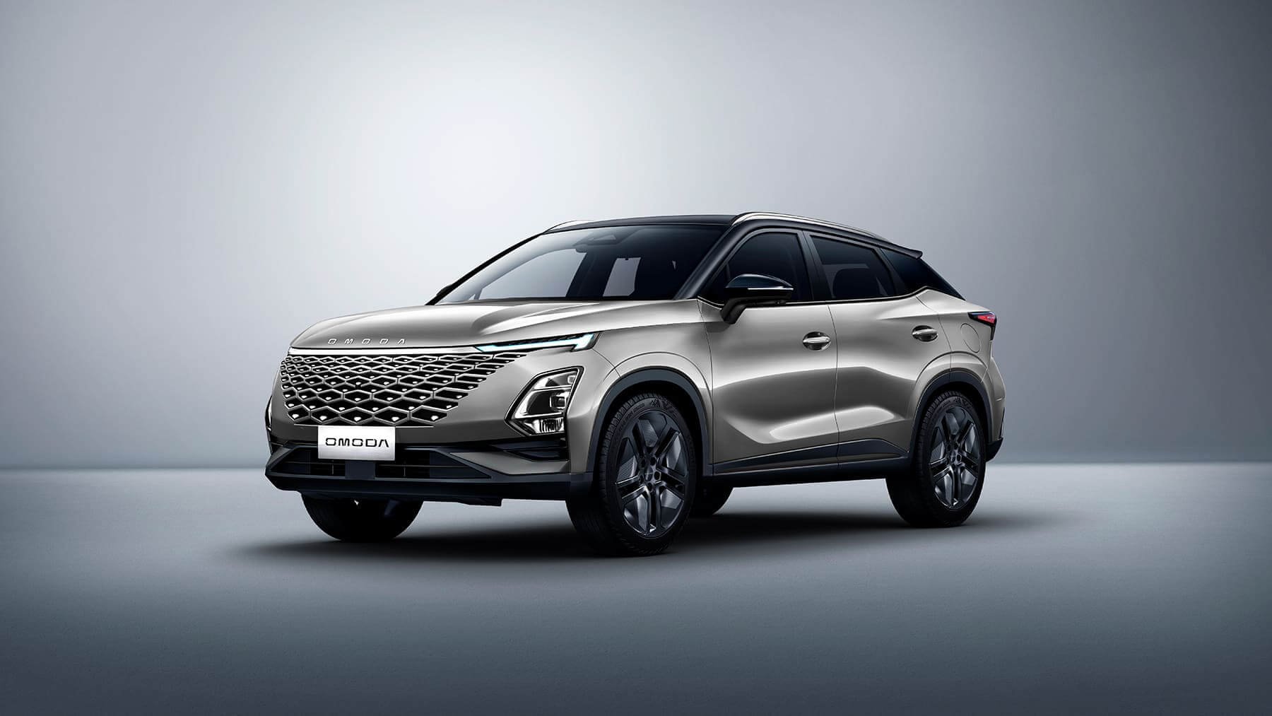 Fotografía promocional del SUV Omoda 5 en color plata metalizado sobre un fondo gris neutro. El vehículo se muestra en ángulo tres cuartos delantero, destacando su diseño moderno con una llamativa parrilla frontal en patrón diamante, faros LED angulares, línea de techo tipo coupé con techo negro contrastante, y llantas de aleación deportivas. La carrocería presenta líneas fluidas y dinámicas con marcados pliegues laterales. El diseño general transmite una imagen premium y deportiva característica de los SUV crossover contemporáneos.