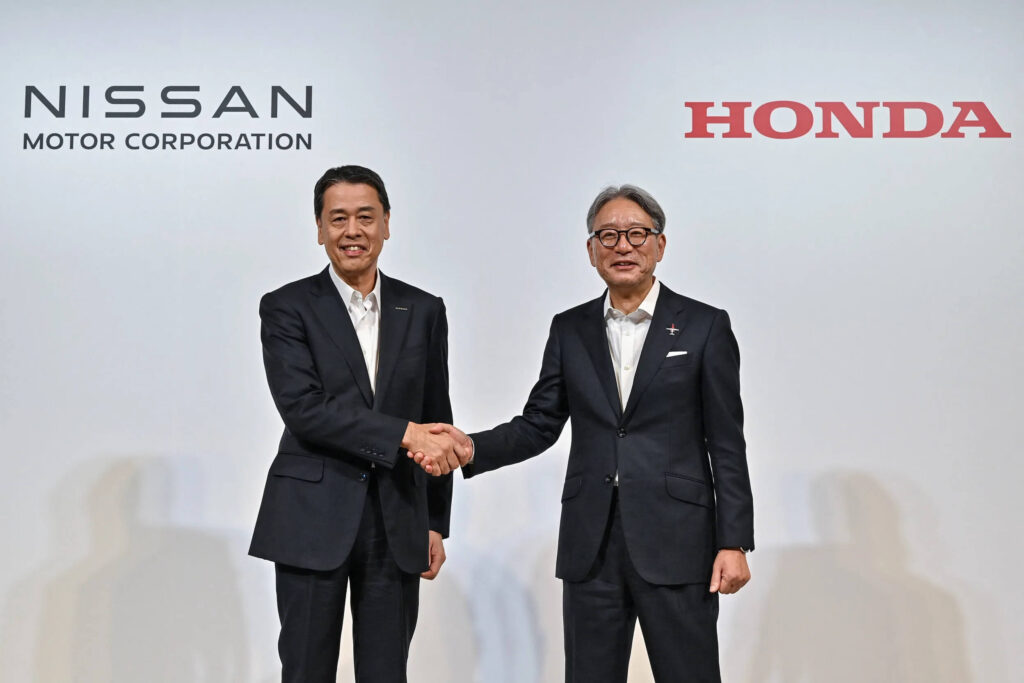 Imagen de dos personas dándose la mano frente a un fondo con los logotipos de Nissan Motor Corporation y Honda. Esta imagen es relevante ya que probablemente representa una asociación o colaboración significativa entre las dos grandes compañías automotrices, Nissan y Honda. El apretón de manos simboliza acuerdo y cooperación, lo que podría tener importantes implicaciones para la industria automotriz.