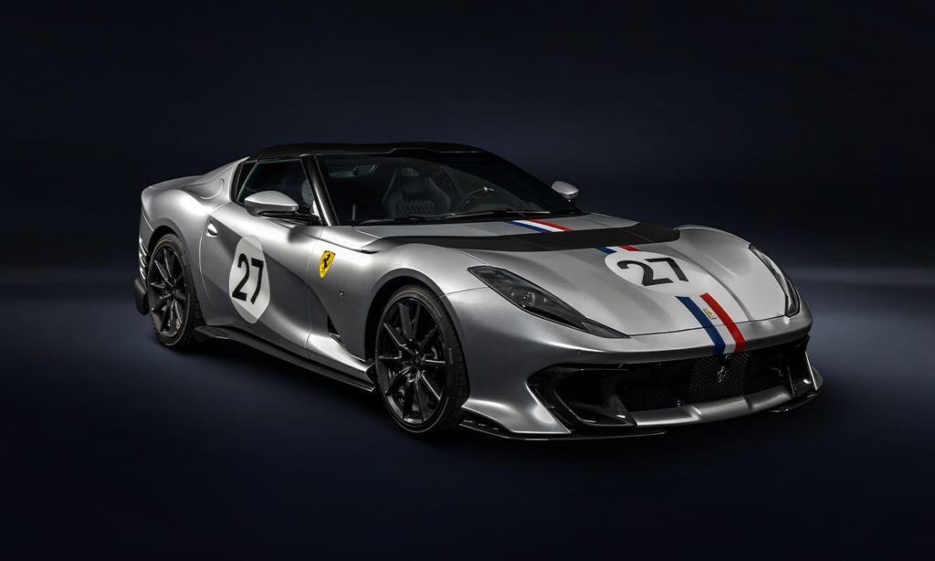 La imagen muestra un Ferrari Competizione A personalizado por Ferrari Tailor Made. El coche es de color plateado con detalles en negro y tiene el número 27 en un círculo blanco en el capó y en las puertas laterales. También presenta una franja tricolor (rojo, blanco y azul) que recorre el centro del vehículo desde el capó hasta la parte trasera. El logotipo de Ferrari está visible en el lateral del coche. El diseño aerodinámico y los detalles de alta gama destacan en esta imagen, mostrando la exclusividad y personalización que ofrece el programa Tailor Made de Ferrari.