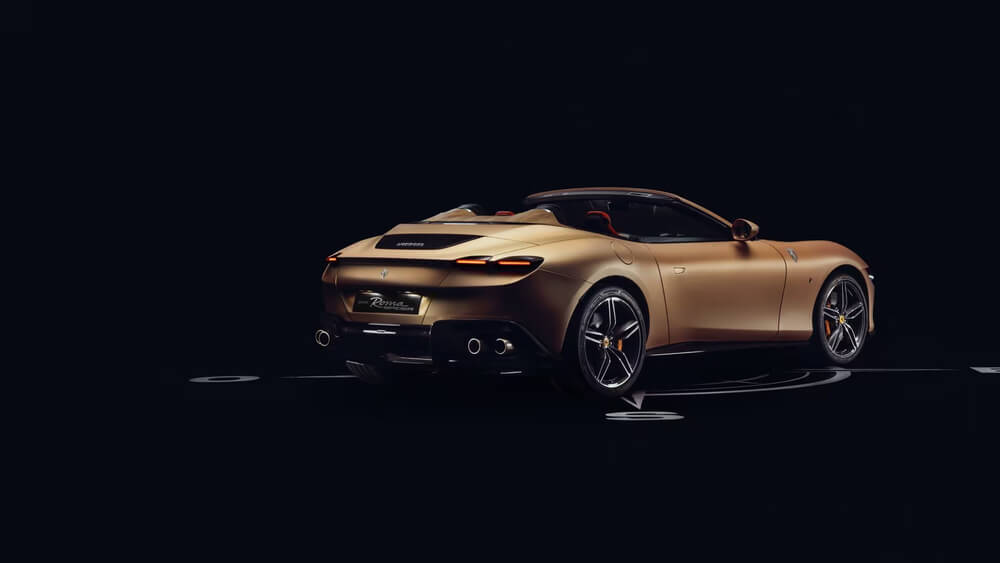 La imagen muestra un Ferrari Roma descapotable en un color dorado mate, visto desde un ángulo trasero derecho. El coche tiene un diseño elegante y deportivo, con líneas suaves y aerodinámicas. Se destacan las luces traseras delgadas, el difusor trasero con cuatro tubos de escape y las llantas de aleación con detalles en color dorado. El logotipo de Ferrari es visible en la parte trasera del coche. La imagen es interesante y relevante porque muestra un modelo exclusivo y personalizado de Ferrari, resaltando su diseño y acabados de alta calidad.