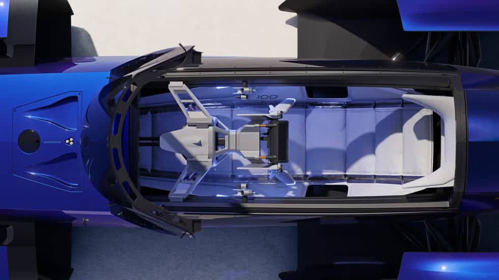 Vista superior del interior de un vehículo futurista, probablemente un coche conceptual. El vehículo tiene un diseño moderno y elegante con un exterior azul y una cúpula transparente. El interior cuenta con un solo asiento y un interfaz de control de alta tecnología, incluyendo una pantalla central y varios elementos de control. El diseño es minimalista y enfatiza la tecnología avanzada, sugiriendo un enfoque en soluciones de movilidad futuras.