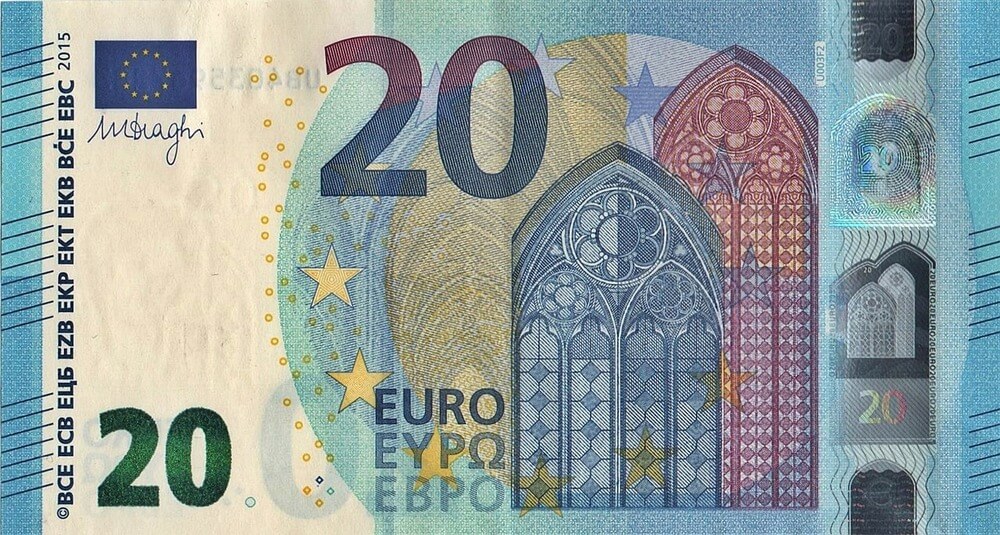 La imagen muestra un billete de 20 euros. El billete tiene varios elementos de seguridad, incluidos una banda holográfica a la derecha, una marca de agua y un hilo de seguridad. El diseño incluye elementos arquitectónicos que recuerdan a ventanas góticas, estrellas que representan la Unión Europea y la denominación "20" destacada en varios lugares. El texto "EURO" y "EYPO" (euro en griego) también es visible. La firma de Mario Draghi, el expresidente del Banco Central Europeo, está presente en el lado izquierdo. El billete es interesante y relevante ya que representa la moneda utilizada por los países de la zona euro e incluye múltiples características de seguridad para prevenir la falsificación.