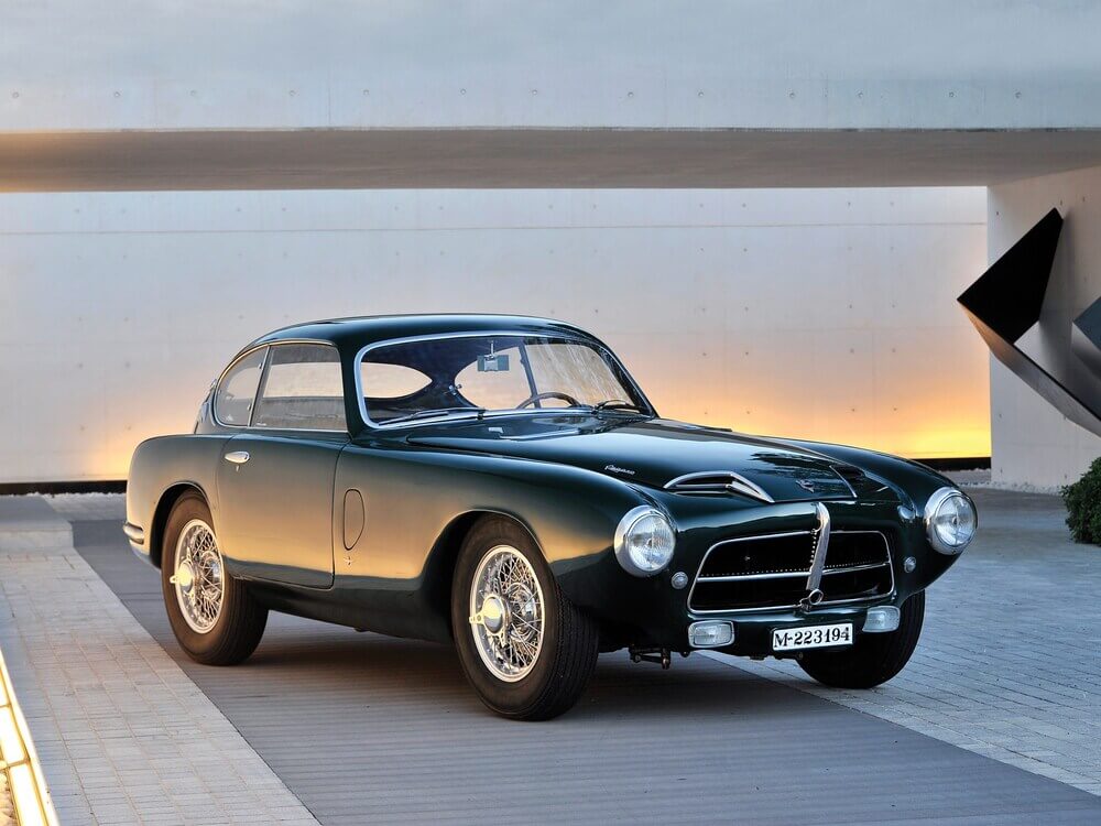 Un automóvil deportivo clásico Pegaso Z-102, producido en España en la década de 1950. Es de color verde oscuro, con un diseño elegante y aerodinámico, y llantas de radios cromados. La matrícula del coche es 'M-223194'. Este modelo es icónico por su exclusividad y su avanzada ingeniería para su época.
