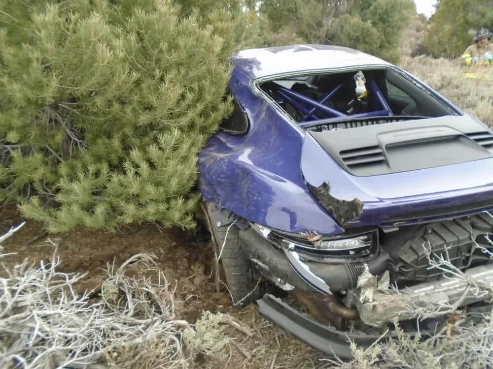 Porsche 911 color morado al fondo de un terraplén. Falta el paragolpes trasero y los pilotos traseros están reventados. La luneta trasera también falla.
