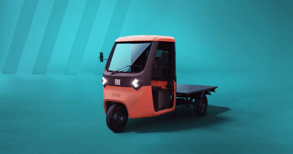 La imagen muestra un isocarro FIAT clásico, un pequeño vehículo de tres ruedas con un diseño compacto y nostálgico. Su carrocería es de color rojo brillante con detalles cromados, evocando un estilo vintage. La cabina es cerrada, y la parte trasera está destinada al transporte de mercancías o pasajeros. Se encuentra estacionado en una calle con arquitectura tradicional, lo que resalta su carácter retro y pintoresco.